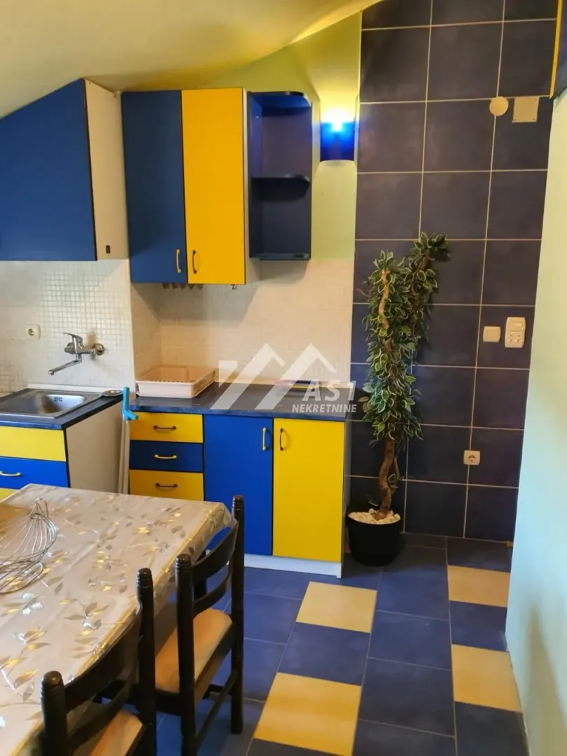Kuhinja sa plavo-žutim elementima i trpezarijskim stolom.