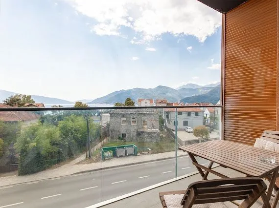 Namješten balkon sa drvenim stolom i stolicama i pogledom na more i planine.