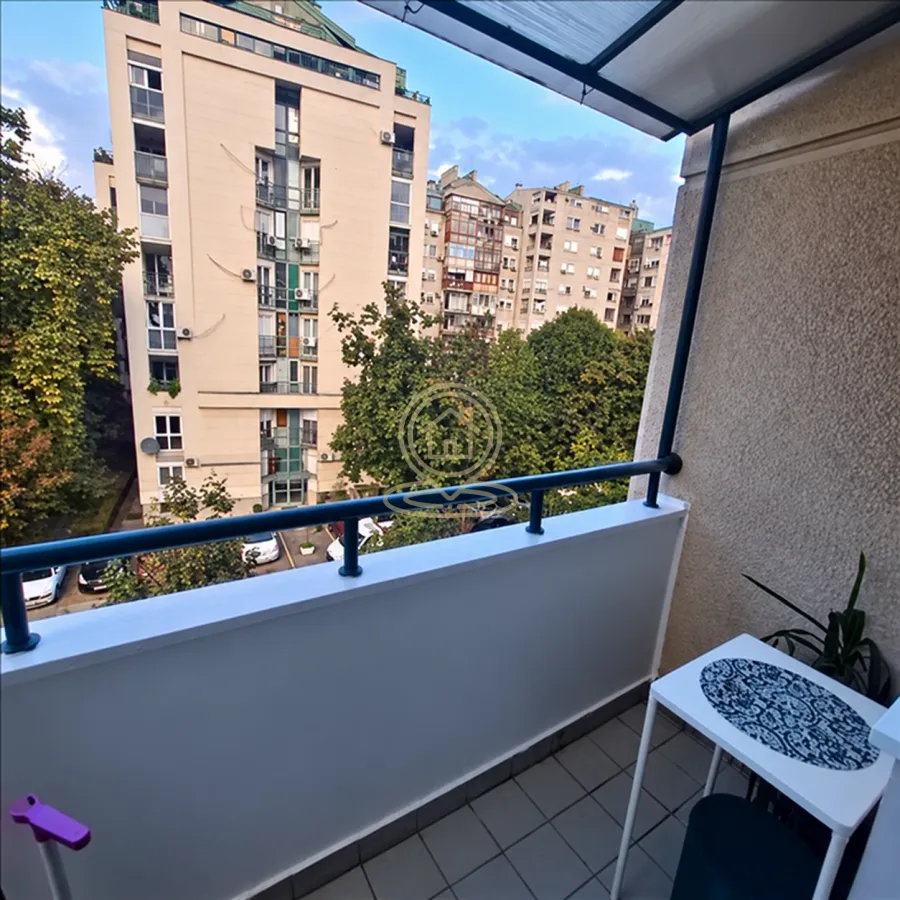 Natkriveni balkon sa pogledom na okolne zgrade i zelenilo.