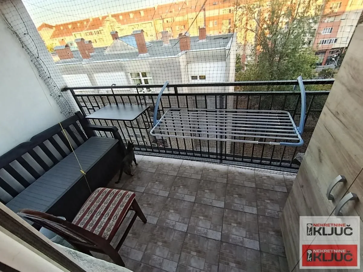 Manji namešten balkon sa garniturom za sedenje i pogledom na okolne zgrade.