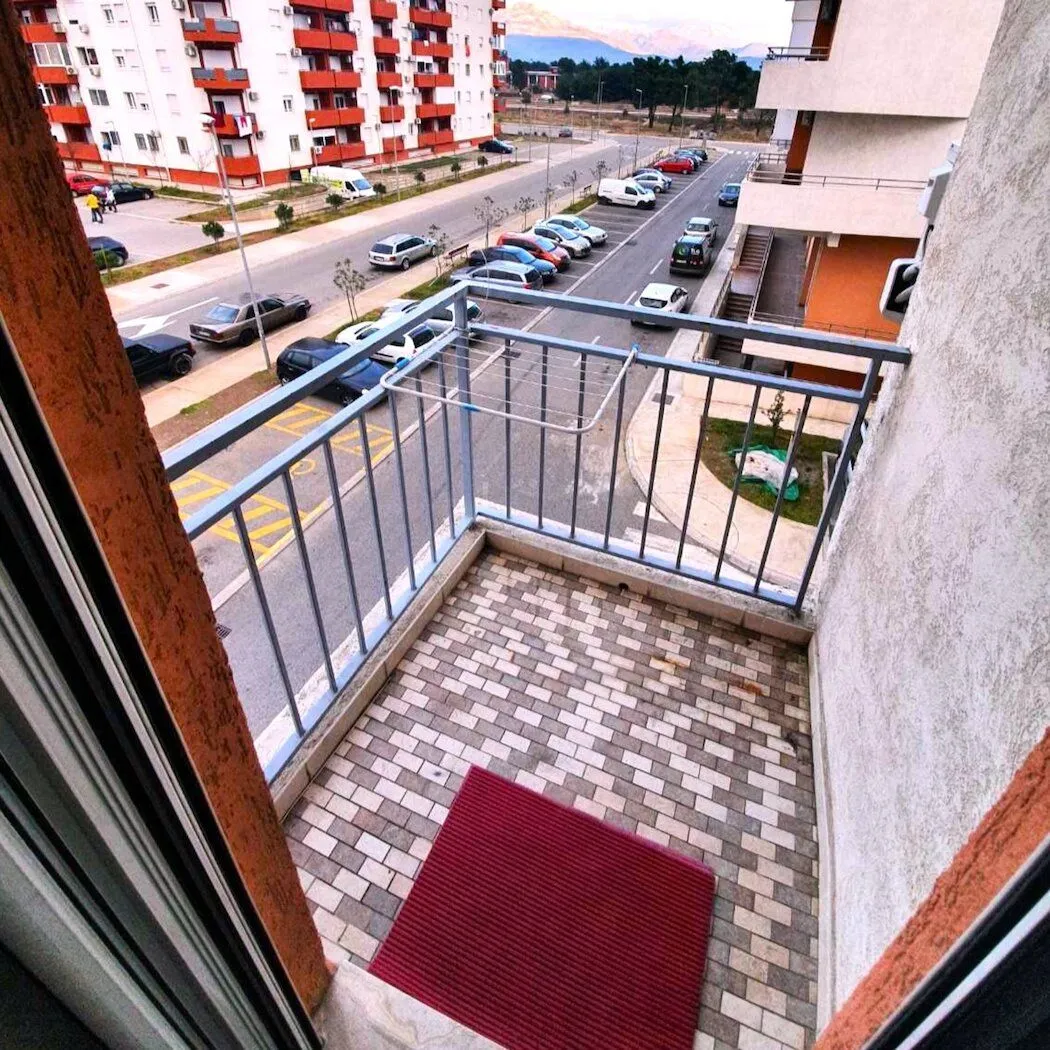 Manji popločani balkon sa ogradom i pogledom na ulicu i parking.