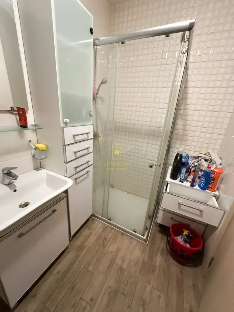 Manje kupatilo sa tuš kabinom, umivaonikom i bijelim elementima.