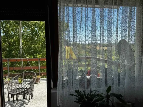 Pogled kroz prozor i vrata na terasu sa visećom stolicom i zelenilom. - image 8