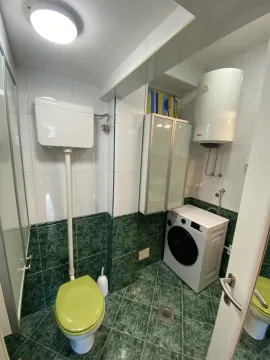 Manje kupatilo sa zelenim pločicama, wc šoljom, veš mašinom i bojlerom. - image 9