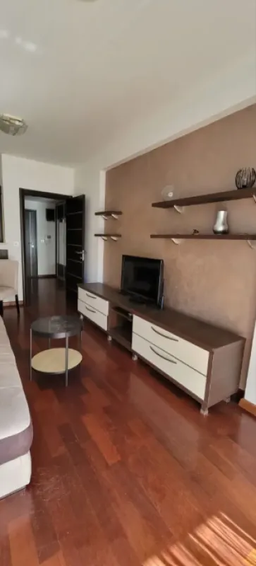 Dnevna soba sa garniturom, TV komodom i policama na zidu.