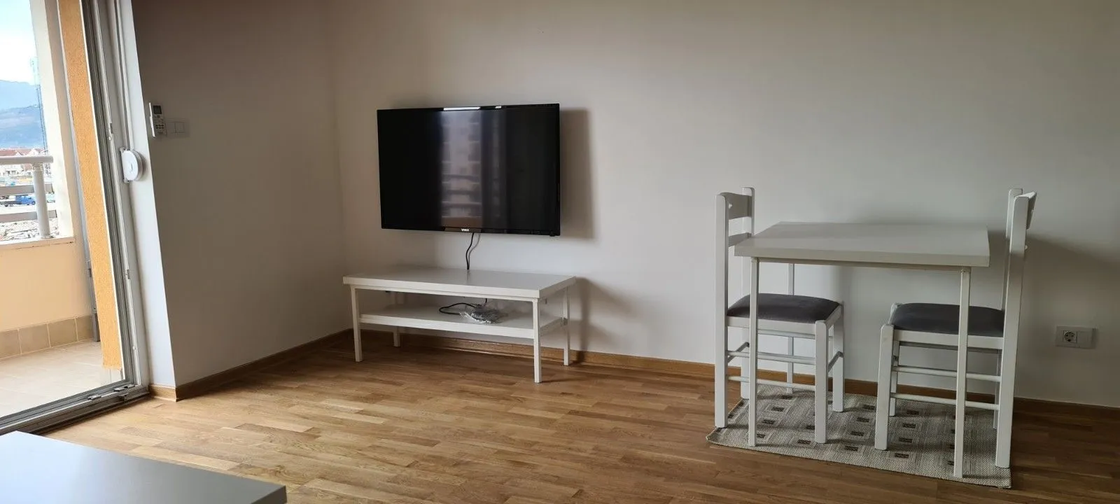 Svijetla dnevna soba sa televizorom i malim stolom za ručavanje.