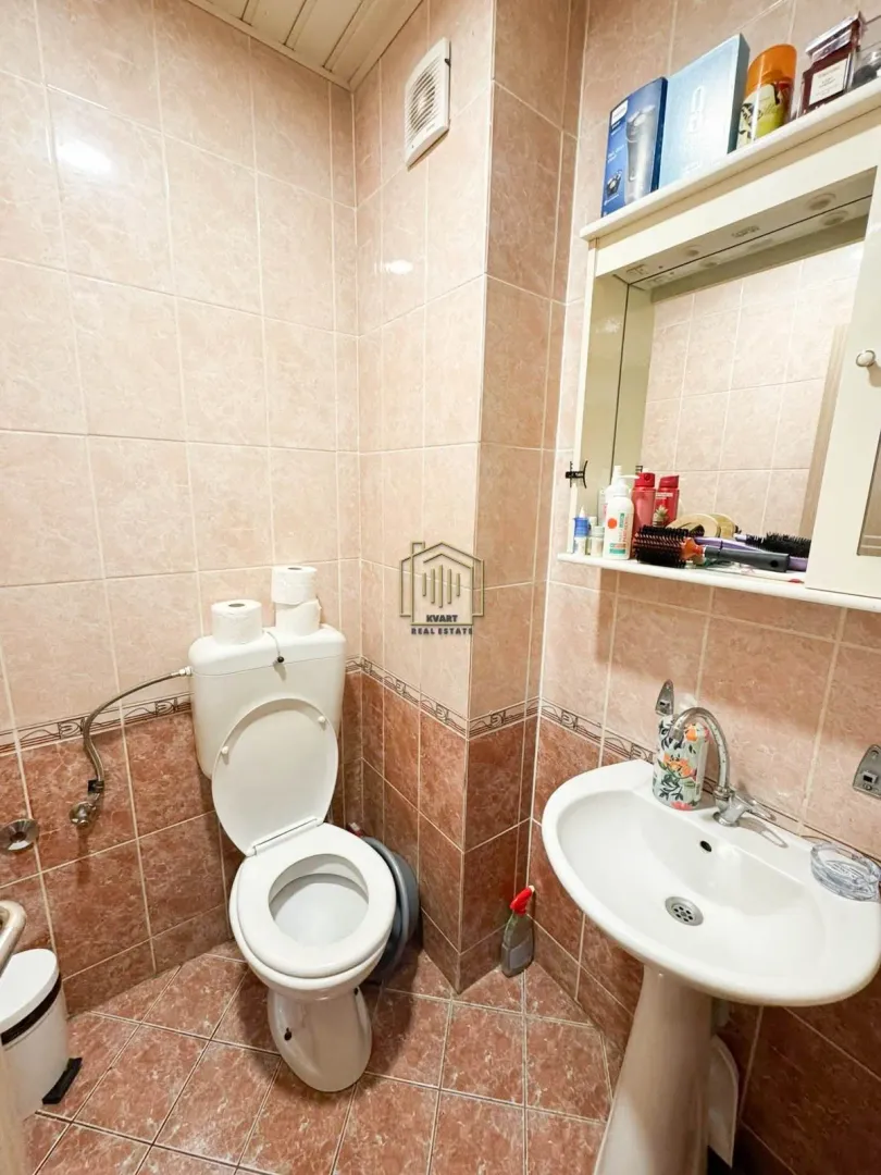 Manje kupatilo obloženo keramičkim pločicama sa WC šoljom, umivaonikom i ogledalom.