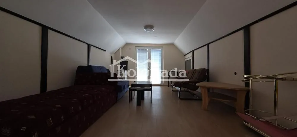 Dnevna soba sa kosim plafonom, kaučem i garniturom za sedenje.