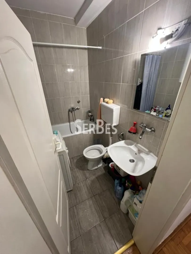 Kompaktno kupatilo sa kadom, umivaonikom i wc šoljom obloženo keramičkim pločicama.