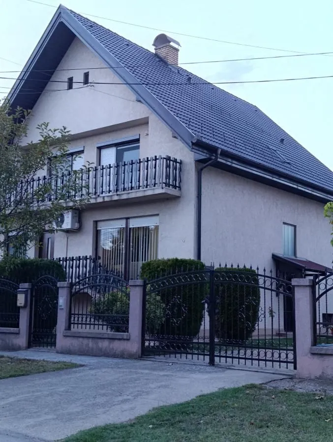 Pogled na spoljašnjost dvospratne kuće sa ograđenim dvorištem i balkonom.