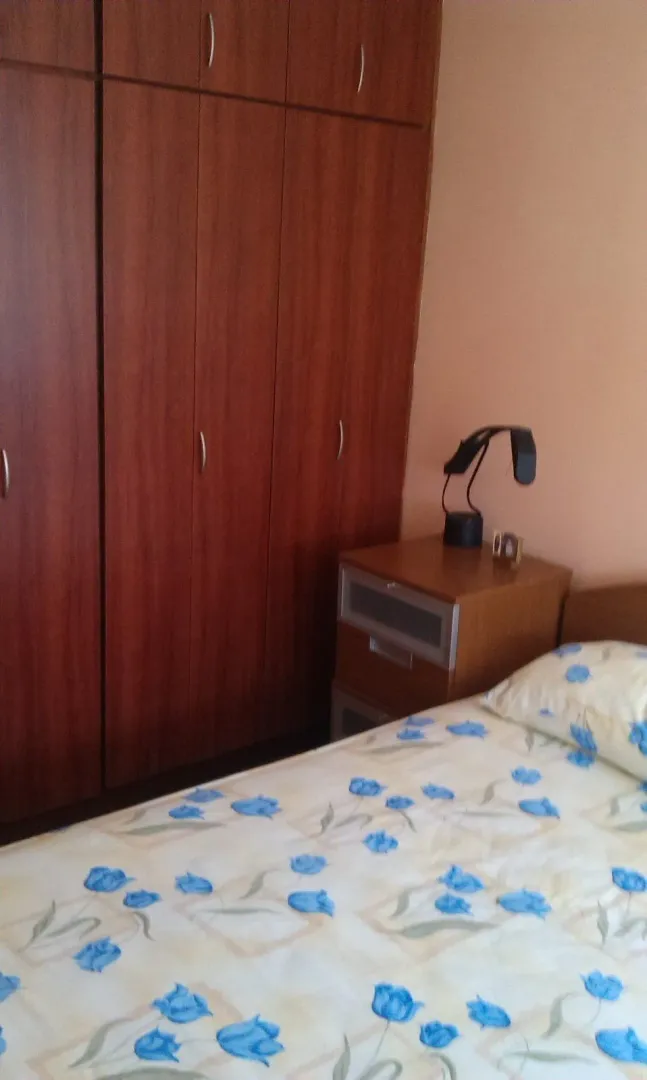 Bedroom with a wooden wardrobe, nightstand, and bed.
