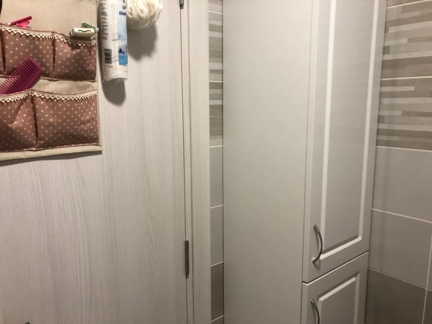 Part of a bathroom with a white cabinet and a wall organizer on the door.