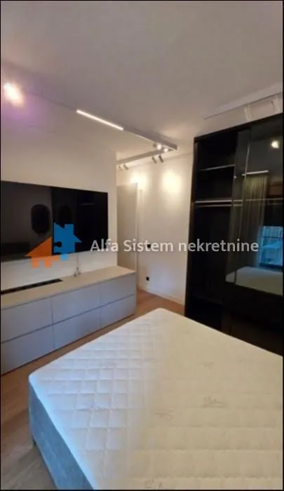 Nameštena spavaća soba sa bračnim krevetom, ormarom i televizorom.