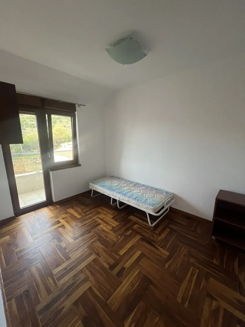 Jednostavna spavaća soba sa parketom i izlazom na balkon.
