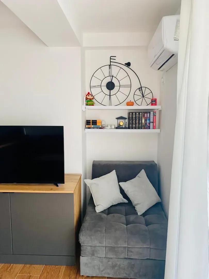 Small corner with an armchair, TV console, and shelving with books and decorations.