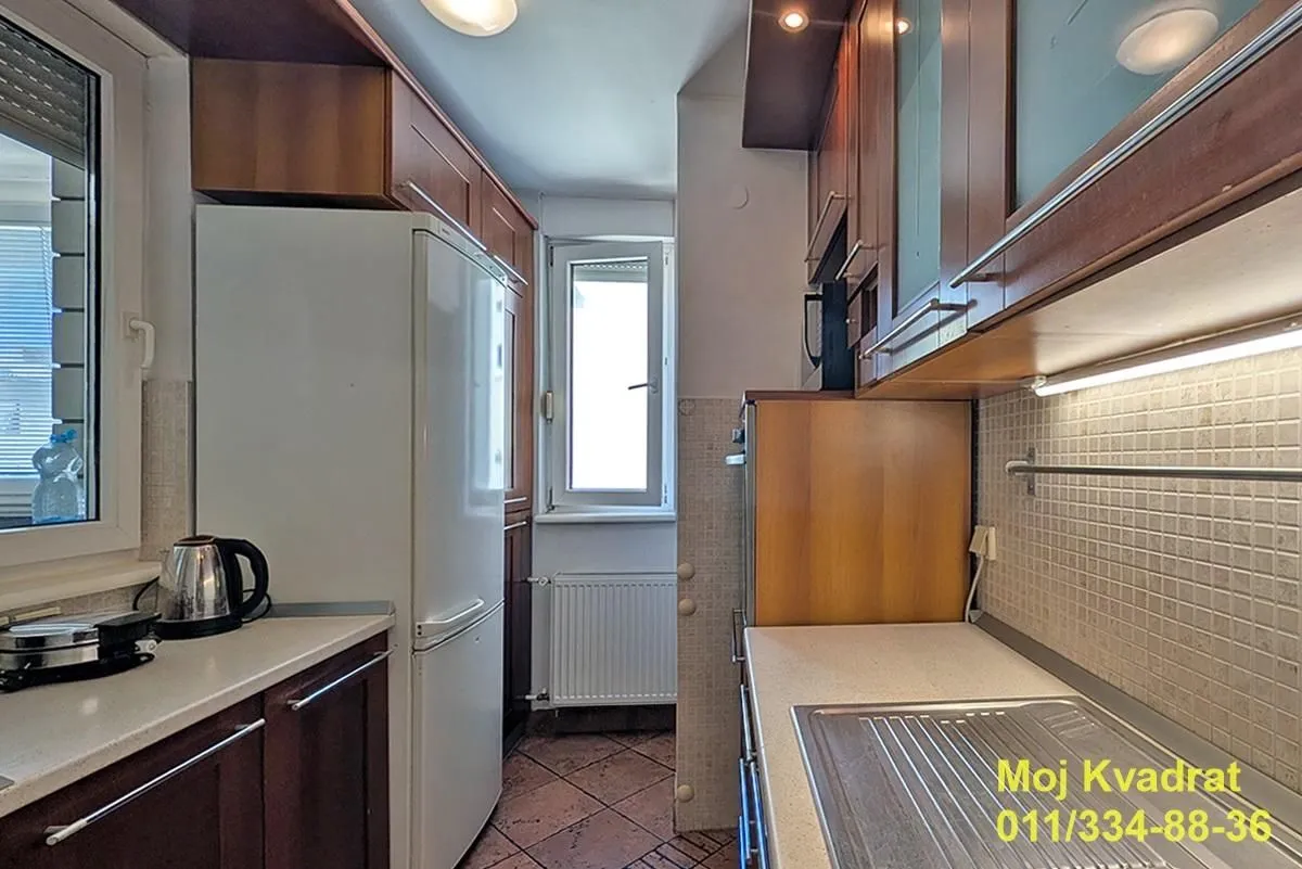 Small kitchen with wooden cabinetry, a refrigerator, and a window at the end of the room.
