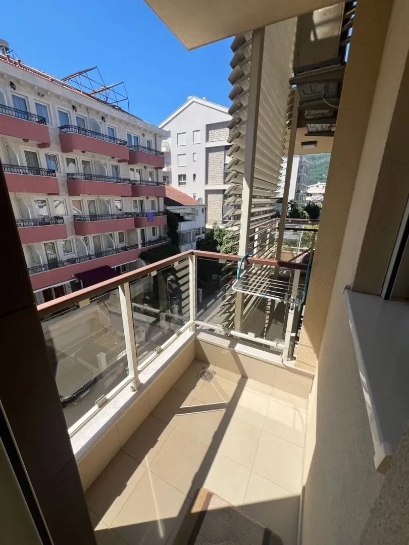 Manji popločani balkon sa staklenom ogradom i pogledom na zgrade.