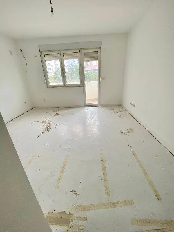 Prazna prostorija sa belim zidovima i prozorom koji gleda na spoljašnjost.