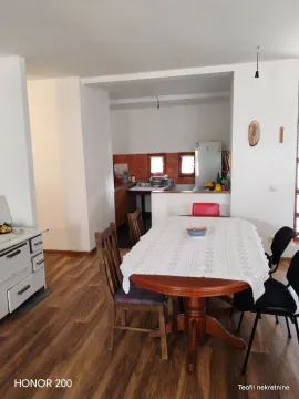 Trpezarija sa drvenim stolom i stolicama i pogledom na kuhinju. - image 3