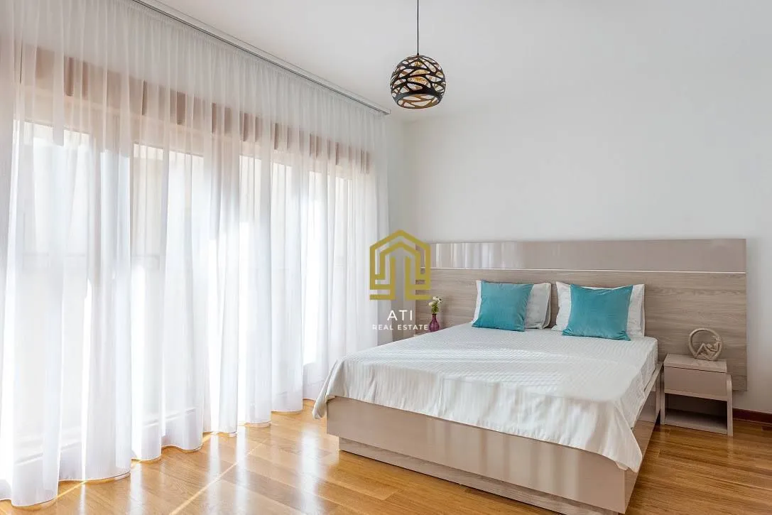 Spacious bedroom with a double bed and a large window with curtains.