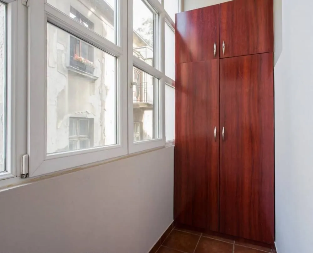 Glazed balcony with a large wooden cabinet and windows overlooking the street.