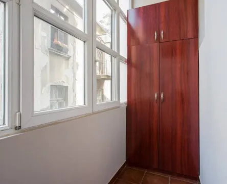 Glazed balcony with a large wooden cabinet and windows overlooking the street. - image 8