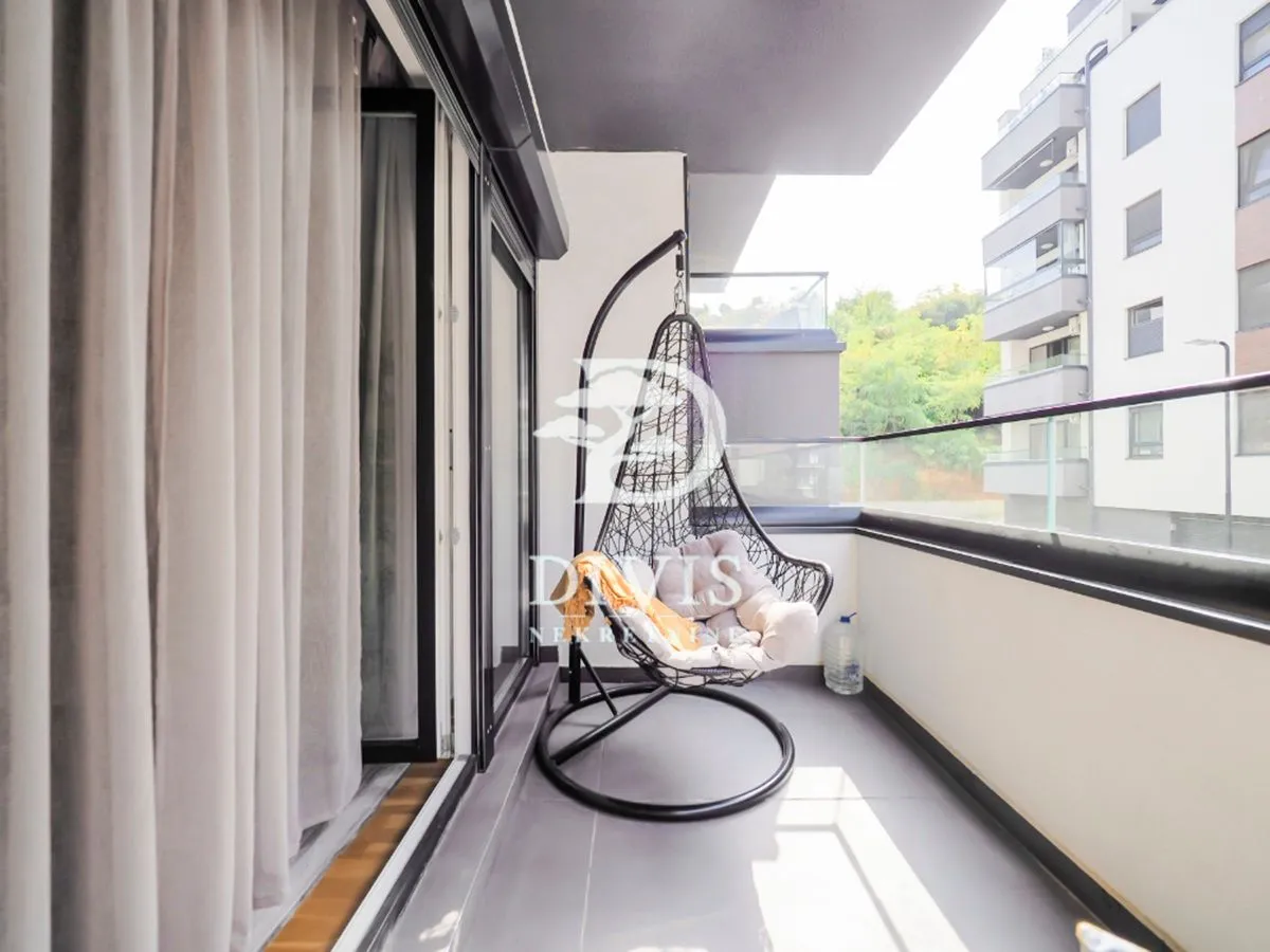 Natkriveni balkon sa visećom foteljom i pogledom na okolne zgrade.