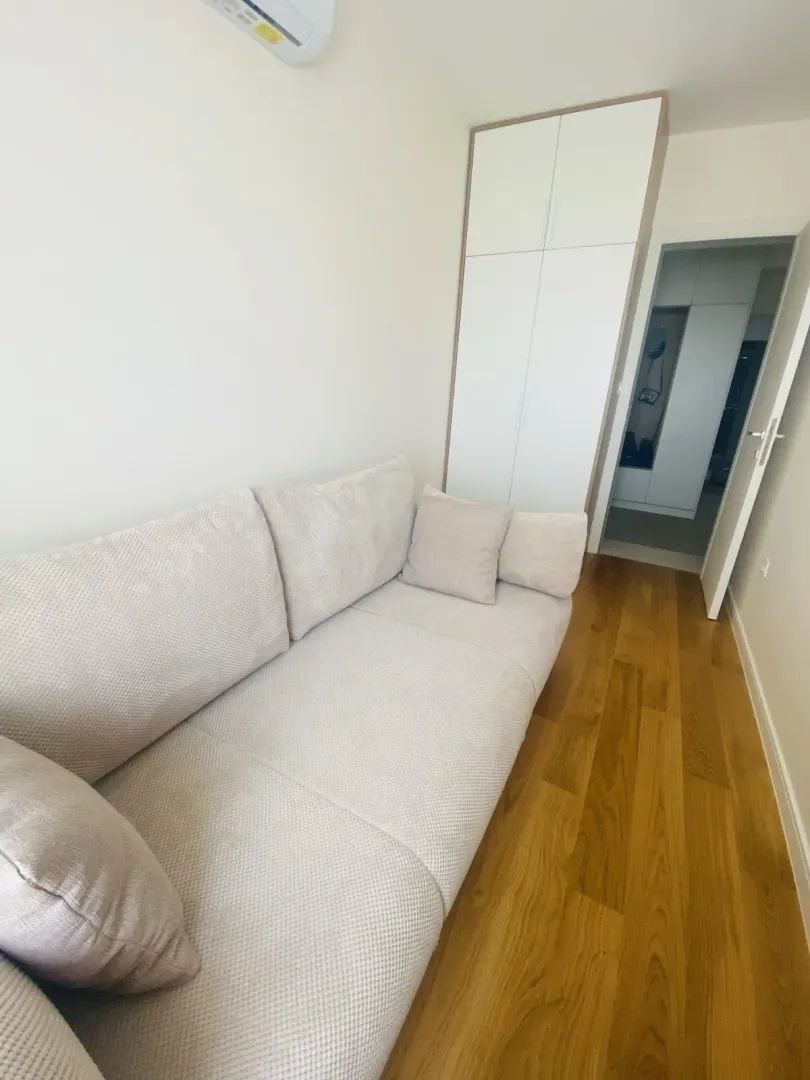 Dnevna soba sa svijetlom garniturom, ugradnim garderoberom i drvenim podom.