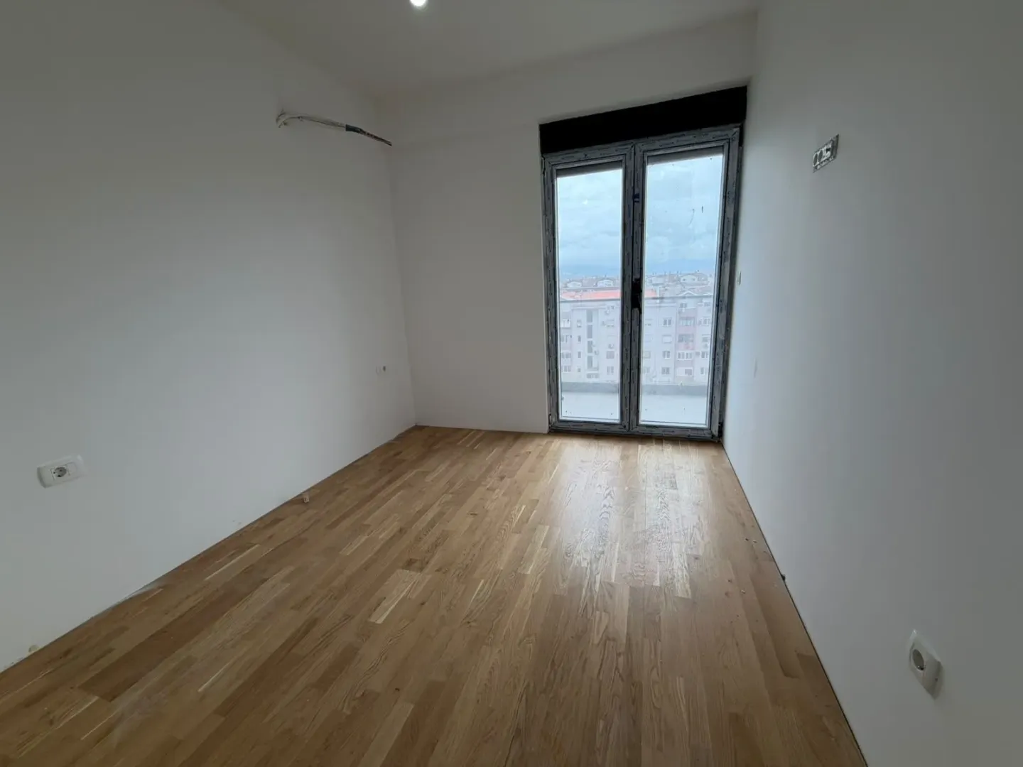 Prazna soba sa drvenim podom i balkonskim vratima.