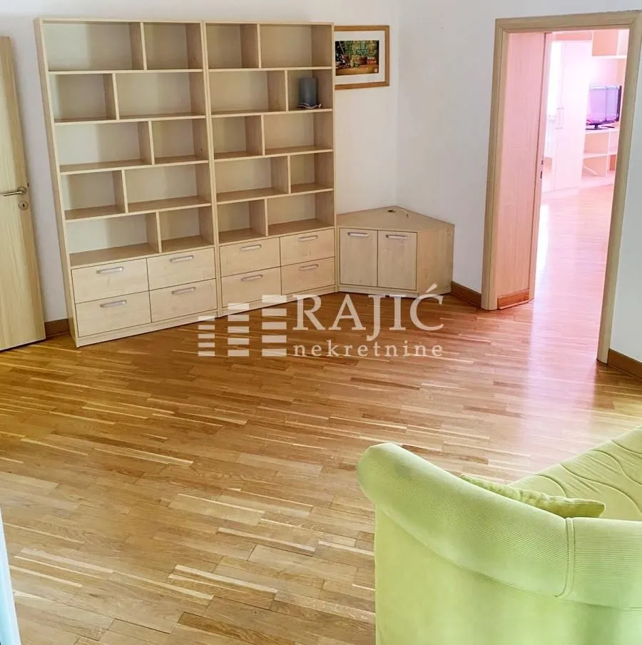 Living room with wooden flooring, a large shelving unit, and a partial view of a sofa.