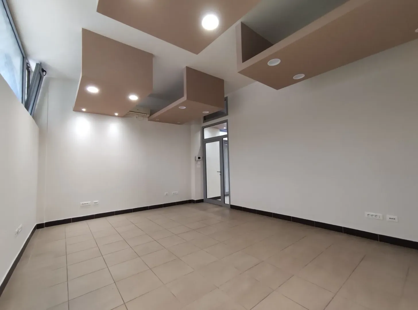 An empty spacious room with tiled flooring and decorative ceiling lighting.