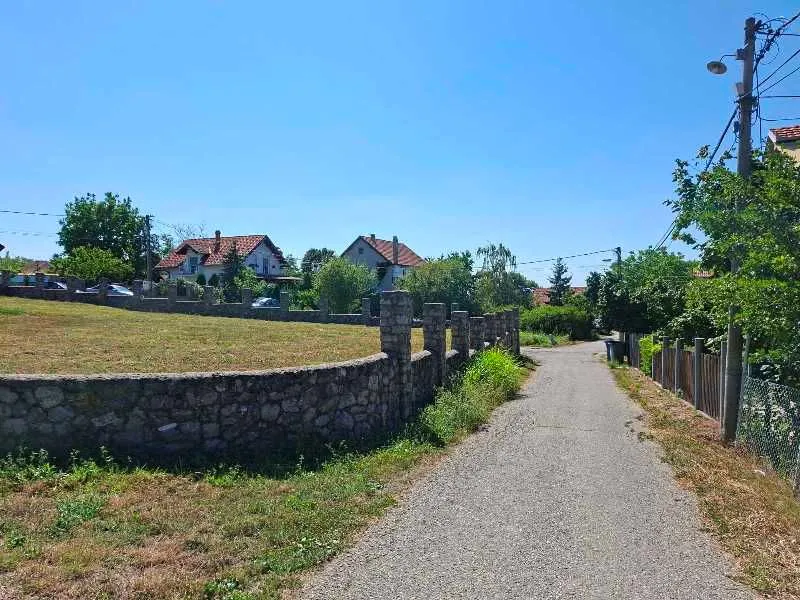 Pogled na prilazni put i plac sa kamenom ogradom u mirnom naselju.