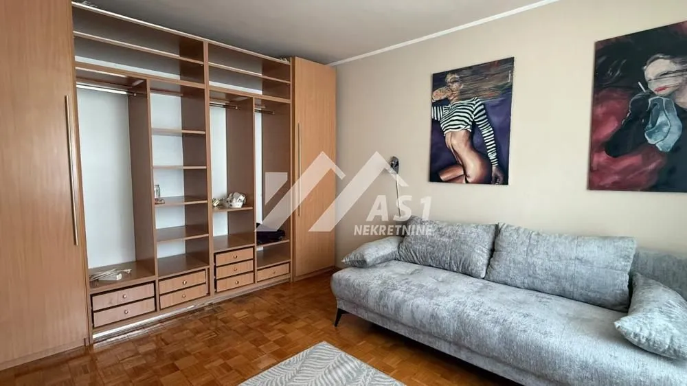 Dnevna soba sa velikim drvenim plakarom, sivim trosedom i slikama na zidu.