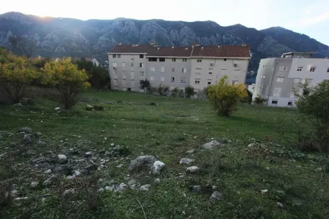 Travnati plac sa stambenim zgradama u pozadini i planinskim vijencem. - image 19