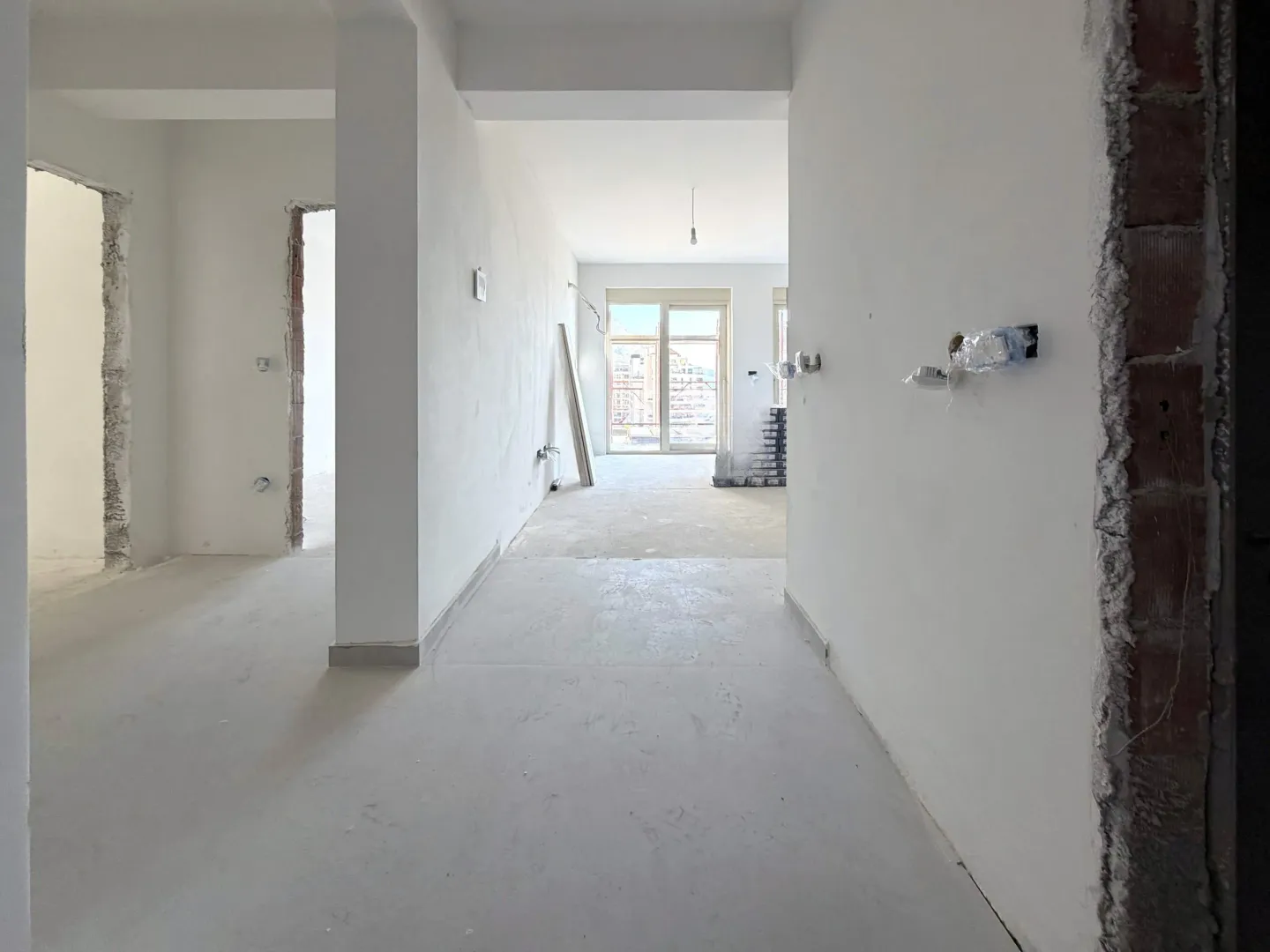 Prazan prostor u stanu u izgradnji sa bijelim zidovima i podom u košuljici.