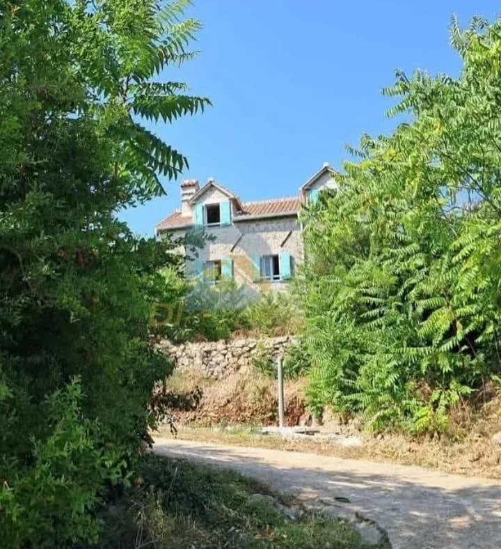 Pogled na kamenu kuću okruženu zelenilom sa pristupnim putem.