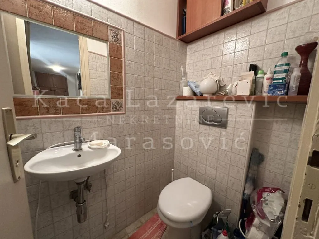 Manje kupatilo obloženo keramičkim pločicama sa umivaonikom, ogledalom i toaletom.