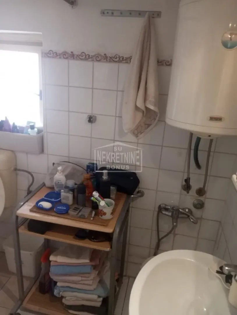 Small bathroom with a sink, water heater, and a shelf with toiletries.