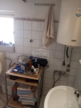 Small bathroom with a sink, water heater, and a shelf with toiletries. - image 4