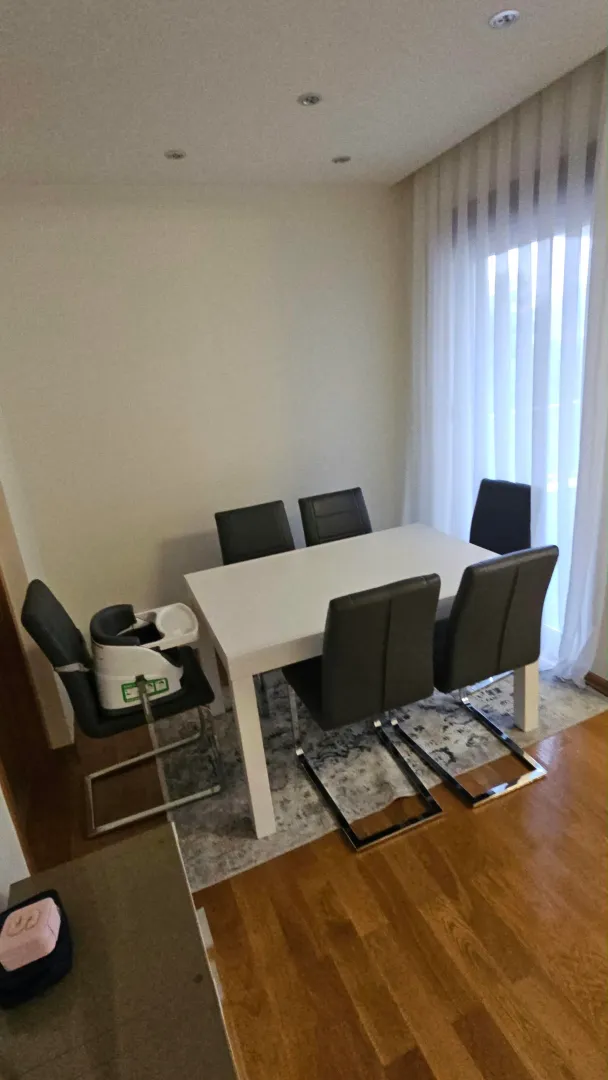 Trpezarija sa bijelim stolom i sivim stolicama pored prozora.
