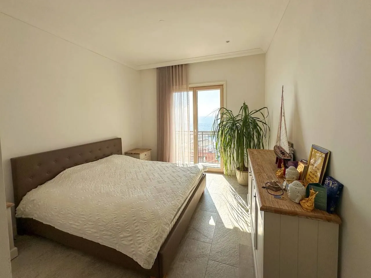 Spavaća soba sa bračnim krevetom, komodom i izlazom na balkon sa pogledom na more.