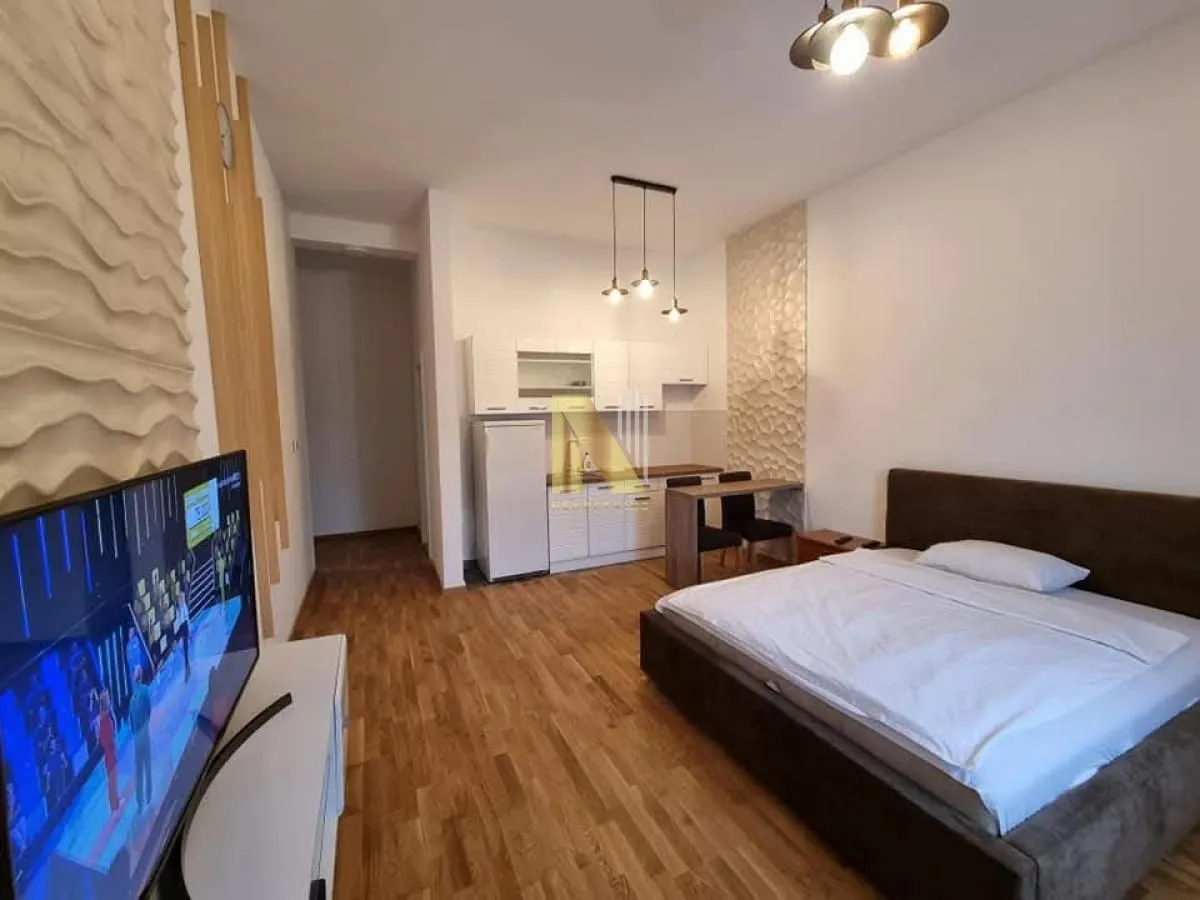Spavaća soba sa bračnim krevetom, televizorom i kuhinjskim kutkom.