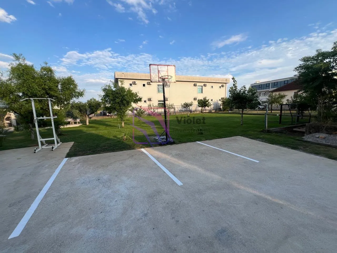 Dvorište sa travnjakom, košarkaškim košem i parking prostorom ispred zgrade.