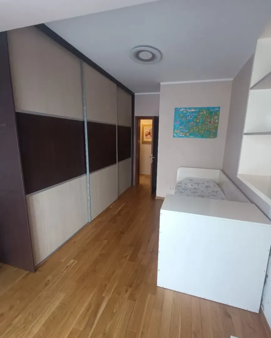 Dječija soba sa krevetom, velikim ugradnim plakarom i parketom na podu.
