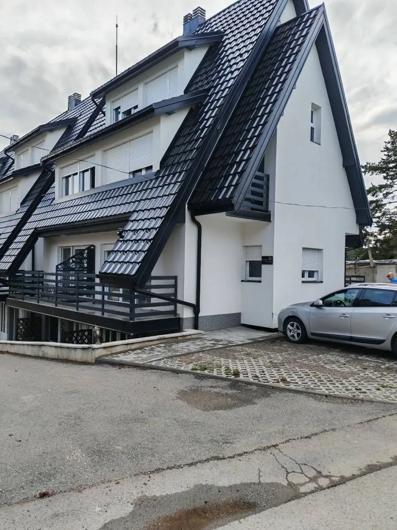 Eksterijer višeporodične kuće sa kosim krovom i dvorišnim parkingom.