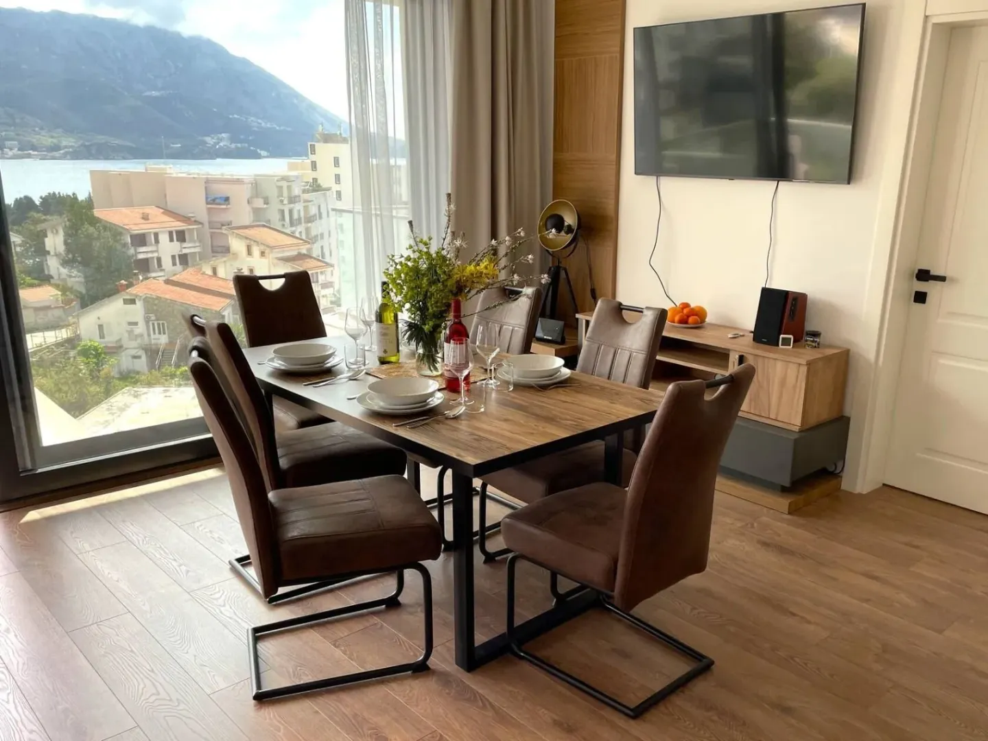 Dining area with a wooden table and chairs, next to a large window with a sea view.