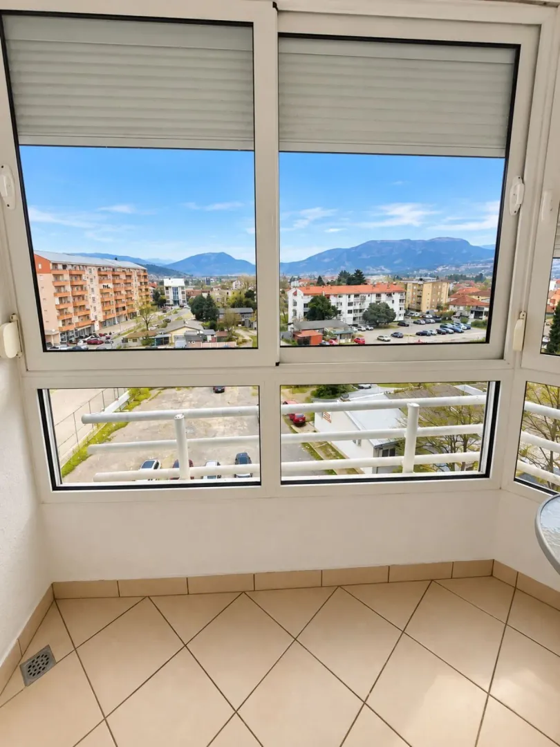 Zastakljeni balkon sa pogledom na grad i okolne planine.