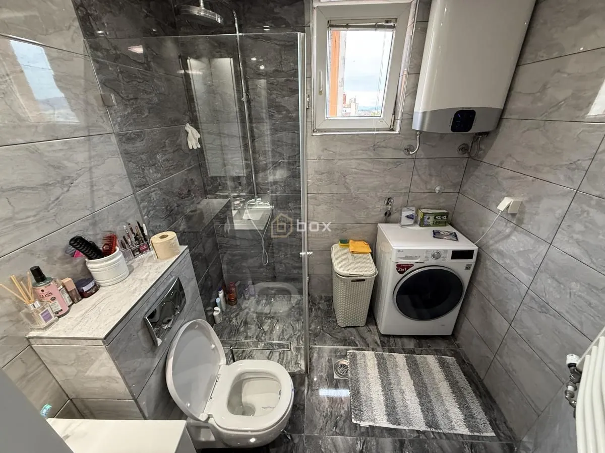 Moderno kupatilo sa tuš kabinom, wc šoljom i veš mašinom.