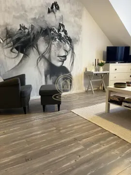 Dnevna soba sa velikom zidnom umetnošću, foteljom i TV komodom pod kosim krovom. - image 15