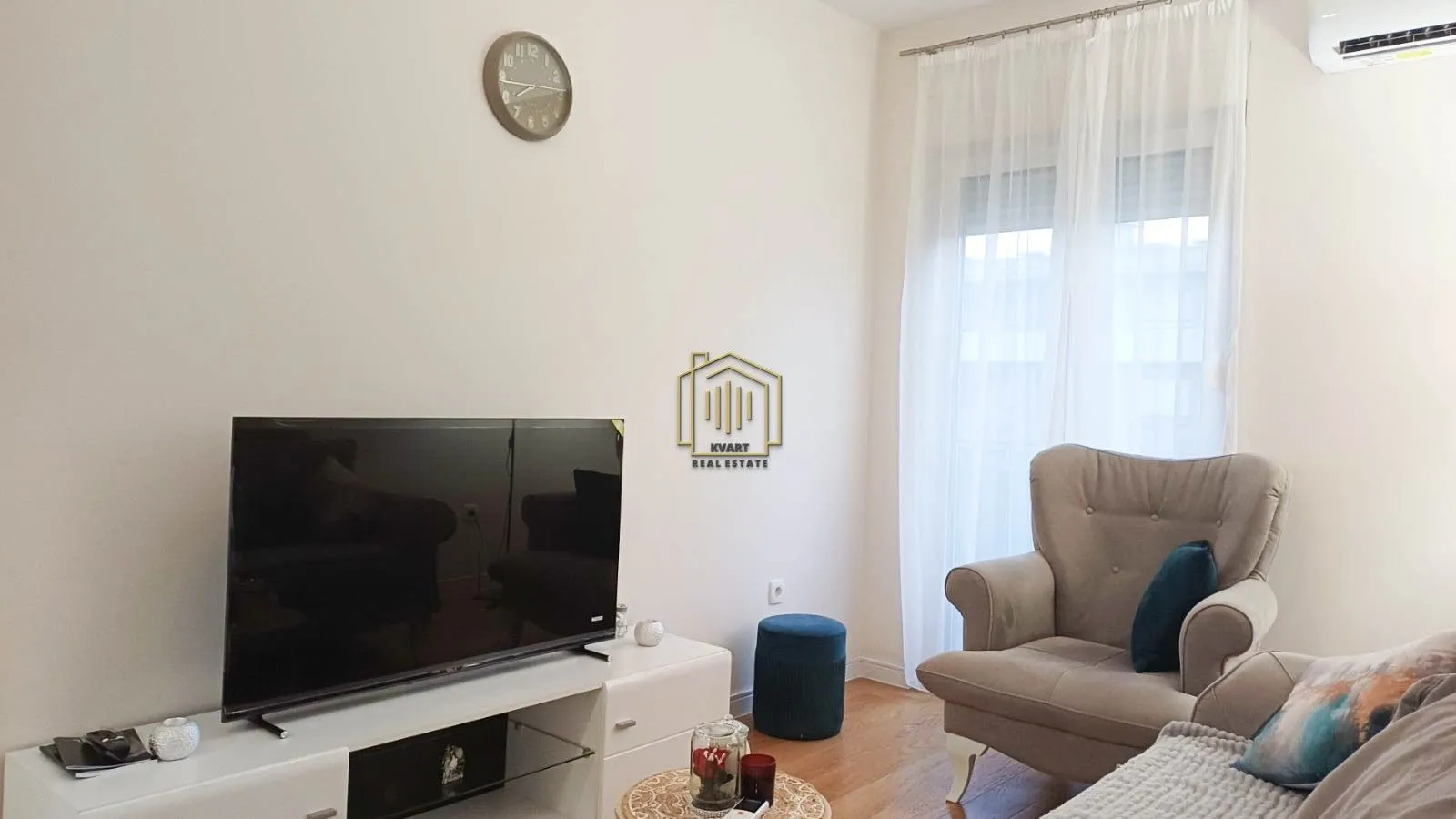 Dnevna soba sa foteljom, TV-om i bijelom komodom.